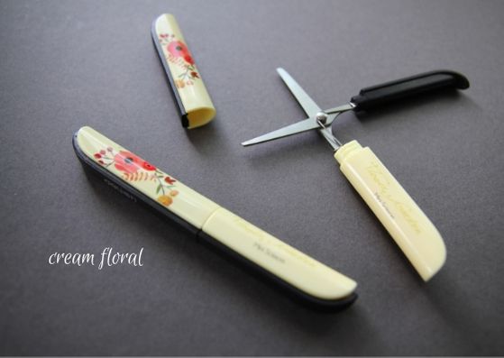 Grey background with two of the floral cream snips.  The bottom snips are lid on and the top have the lid off and blades open.  The flower designs are coral coloured and flow up the lid. 
