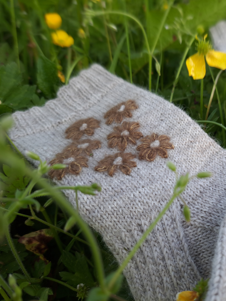 Close up of  Blathan hand knitted Socks in light grey wool with khaki mohair embroidered flowers as a flatlay in a meadow