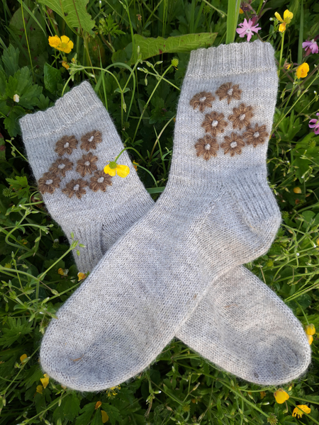 Close up of  Blathan hand knitted Socks in light grey wool with khaki mohair embroidered flowers as a flatlay in a meadow