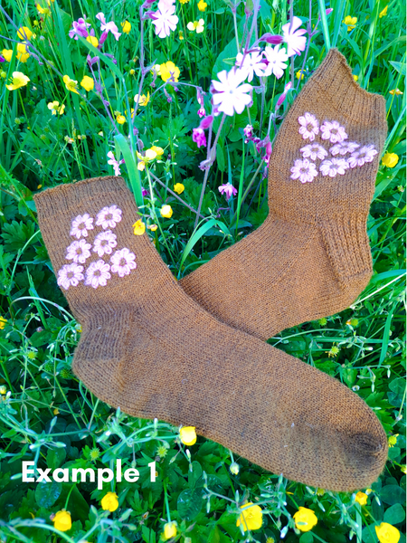 Close up of  Blathan hand knitted Socks in a khaki green with pink embroidered flowers as a flatlay in a meadow