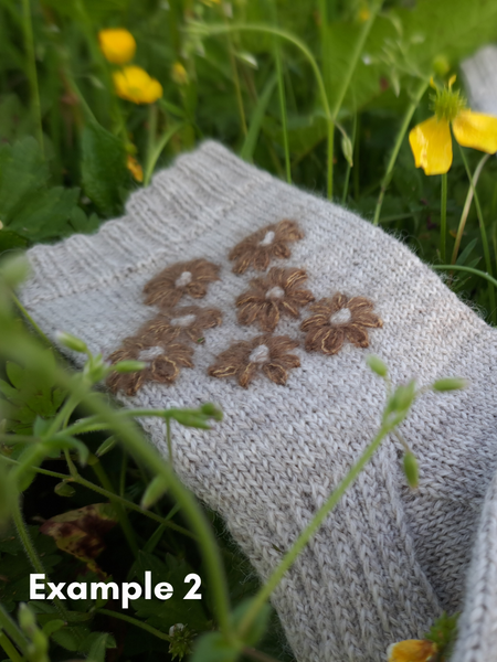 Close up of  Blathan hand knitted Socks in light grey wool with khaki mohair embroidered flowers as a flatlay in a meadow