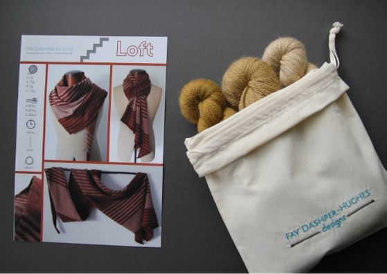 Knit kit for Loft shawl: on left is a hardcopy of the pattern showing the shawl off in three shades of copper and on the right are the three shades of mustard available getting darker from right to left, all sat in a rolled back bag with "Fay Dashper-Hughes Designs" embroidered on it.