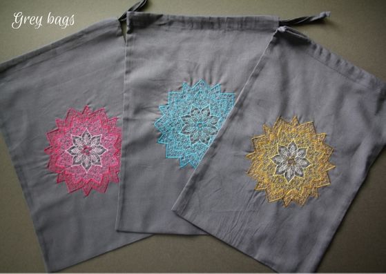 Grey mandala project bags: three grey cotton bags with a mandala on each fading from a dark outside to lighter inner.  L-R the mandalas are pink, turquoise and yellow