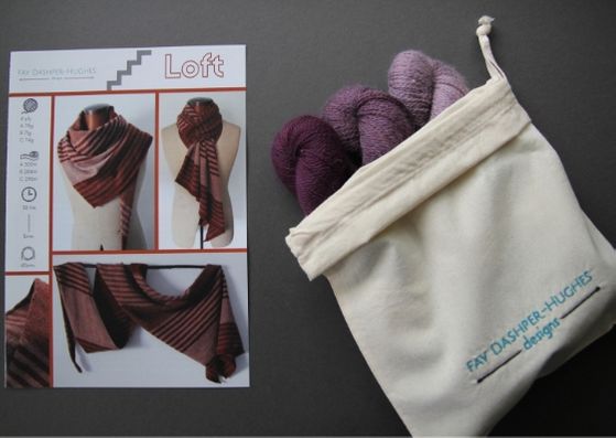Knit kit for Loft shawl: on left is a hardcopy of the pattern showing the shawl off in three shades of copper and on the right are the three shades of plum available getting darker from right to left, all sat in a rolled back bag with "Fay Dashper-Hughes Designs" embroidered on it.