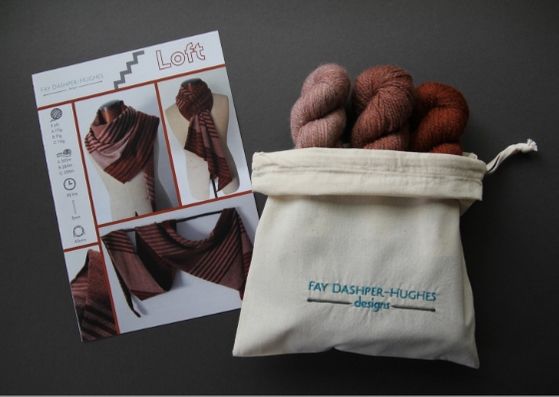 Knit kit for Loft shawl: on left is a hardcopy of the pattern showing the shawl off in three shades of copper and on the right are the three shades of copper available getting darker from right to left, all sat in a rolled back bag with "Fay Dashper-Hughes Designs" embroidered on it.