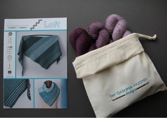 Crochet kit for Loft shawl: on left is a hardcopy of the pattern showing the shawl off in three shades of teal and on the right are the three shades of plum available getting darker from right to left, all sat in a rolled back bag with "Fay Dashper-Hughes Designs" embroidered on it.