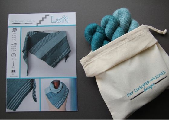 Crochet kit for Loft shawl: on left is a hardcopy of the pattern showing the shawl off in three shades of teal and on the right are the three shades of teal available getting darker from right to left, all sat in a rolled back bag with "Fay Dashper-Hughes Designs" embroidered on it.