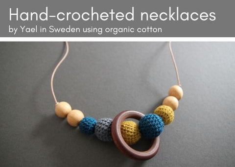 Hand-made crocheted necklace on a grey background. Some wooden beads are threaded onto the leather thng bare and others have been crocheted with organic cotton in grey, dark teal and mustard.  The keather thing is nude in colour.