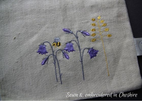 Close up of natural linen bag, embroidered with purple harebells, a yellow sprig of grass and a bumple bee.