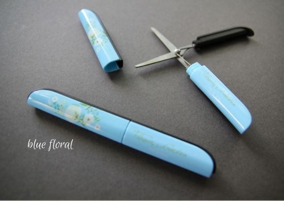 Grey background with two of the floral blue snips.  The bottom snips are lid on and the top have the lid off and blades open.  The flower designs are cream coloured and flow up the lid. 