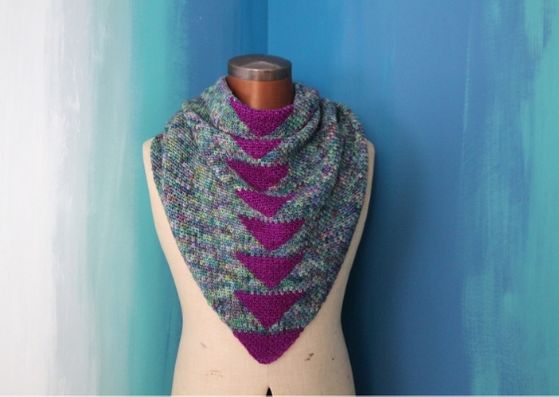 Arria crocheted shawl: The shawl is being worn by a mannequin against a background of blues and teals, painted in a rough vertical fade.