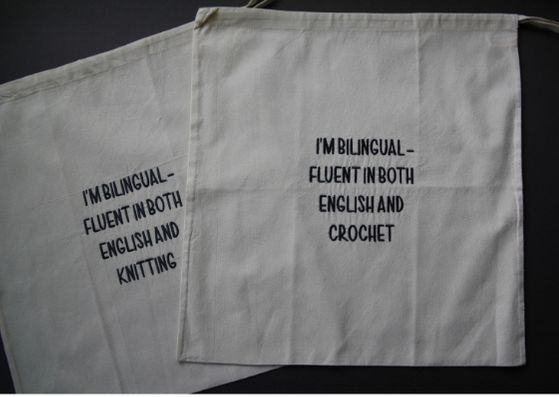 Close up of two natural cotton bags with black text saying " I'm bilingual - fluent in both English and crochet/knit".