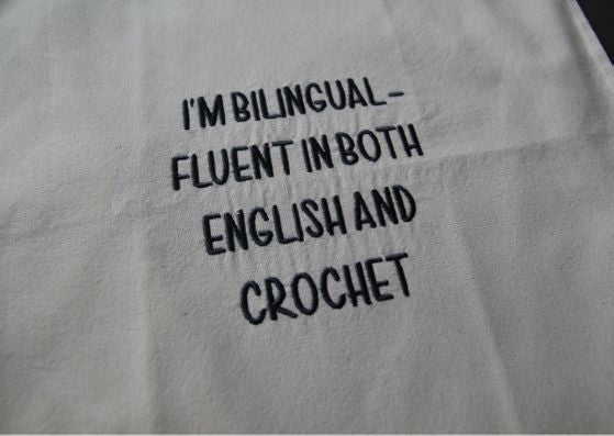 Close up of natural cotton bag with black text saying " I'm bilingual - fluent in both English and crochet".