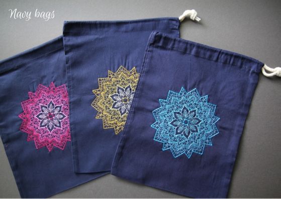 Navy mandala project bags: three navy cotton bags with a mandala on each fading from a dark outside to lighter inner.  L-R the mandalas are pink, yellow and turquoise.